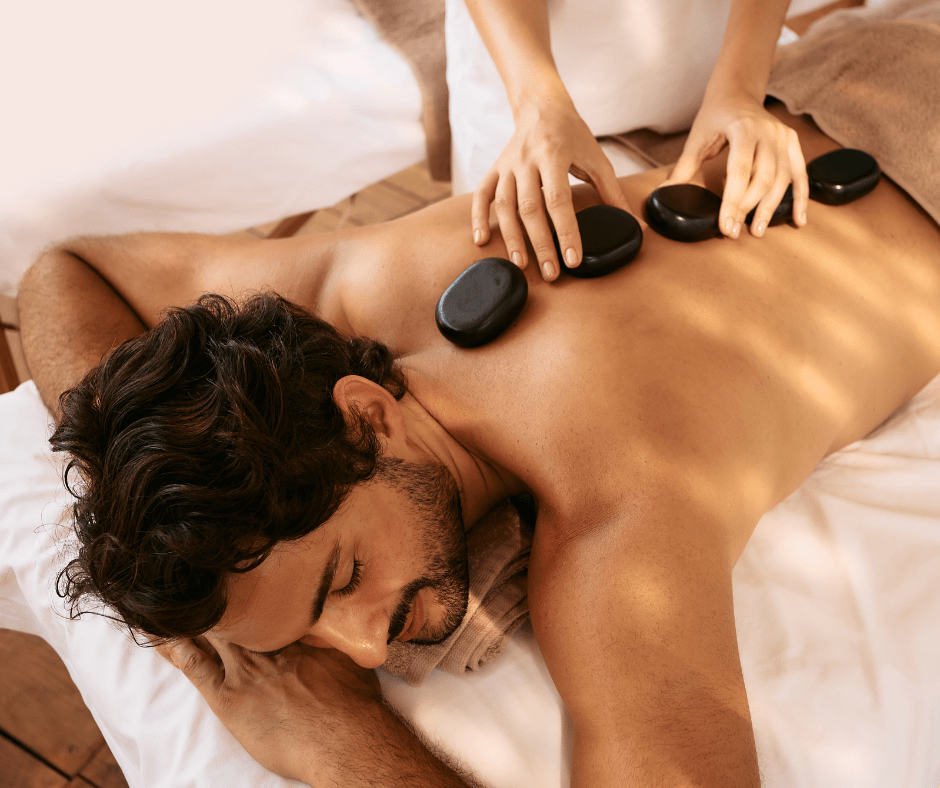 A man lays face down with hot stones for massage on his back, while receiving a professional massage