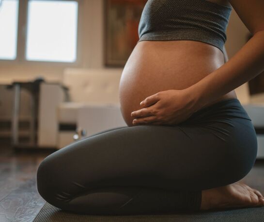 A heavily pregnant woman sits on the ground with her belly displayed