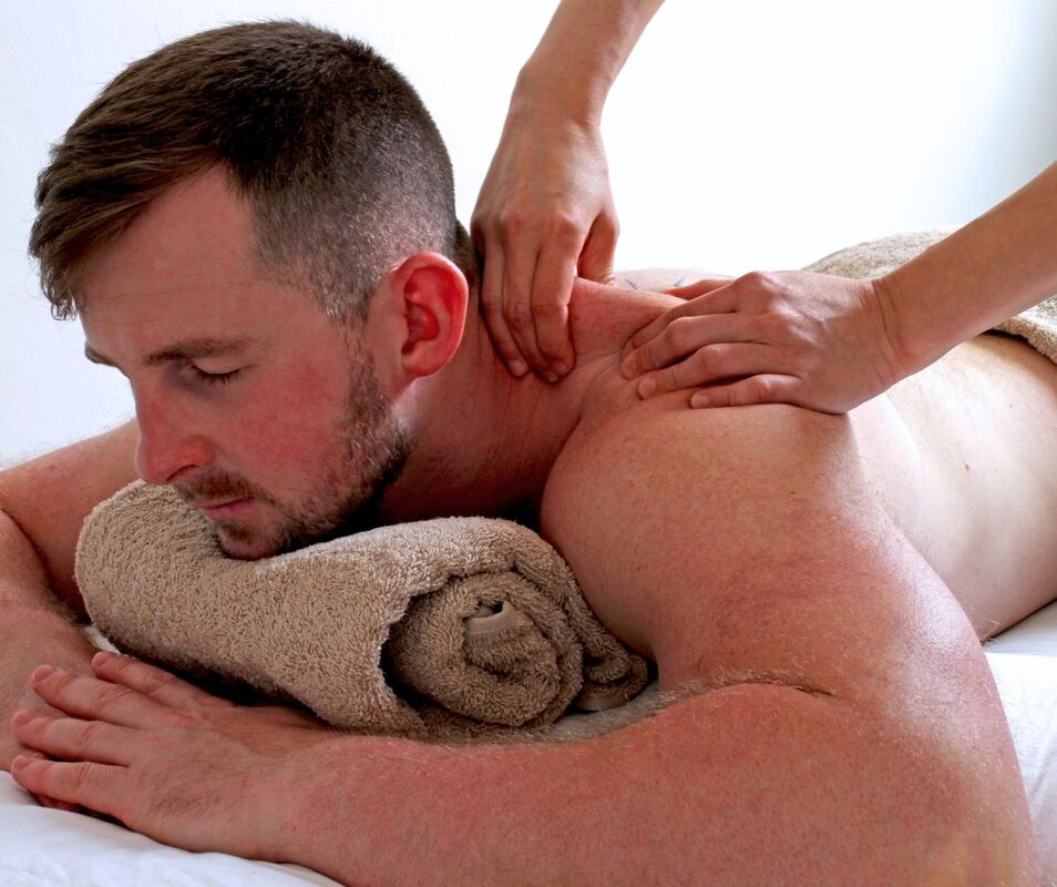A man lies on his stomach and receives a professional massage on his back and shoulders