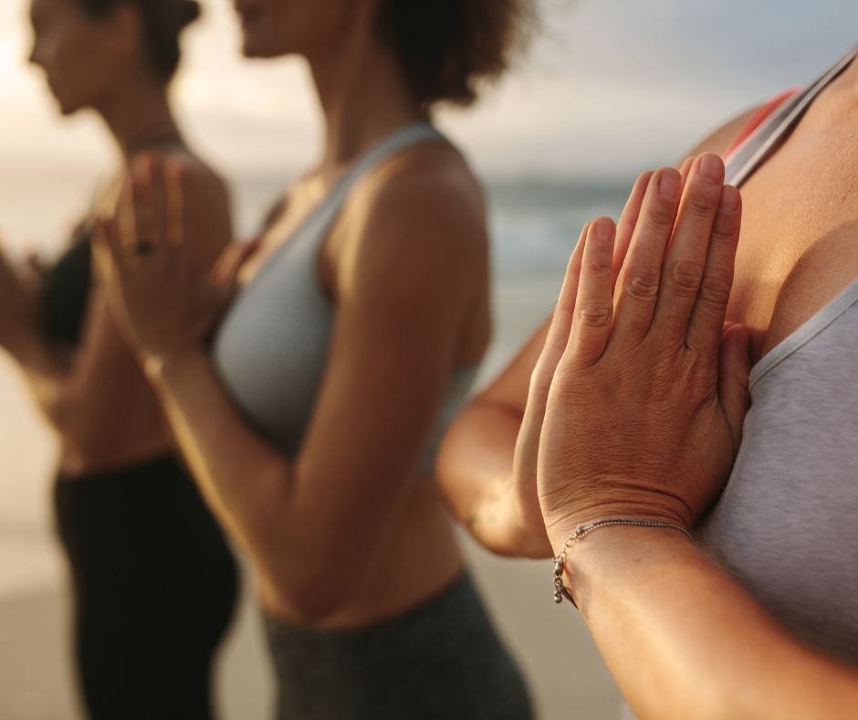 Women practicing yoga and meditation, standing with their hands in prayer position at their heart
